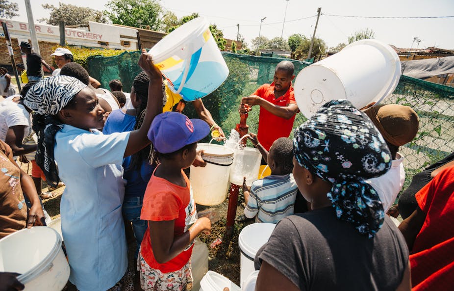 Women and children collect water from a water hydrant. 