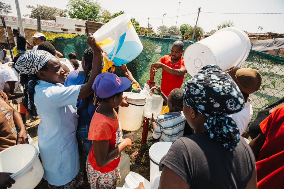 Women and children collect water from a water hydrant. 