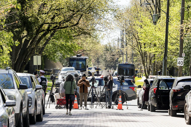 A tree-lined street is jammed with parked police vehicles and television reporters.