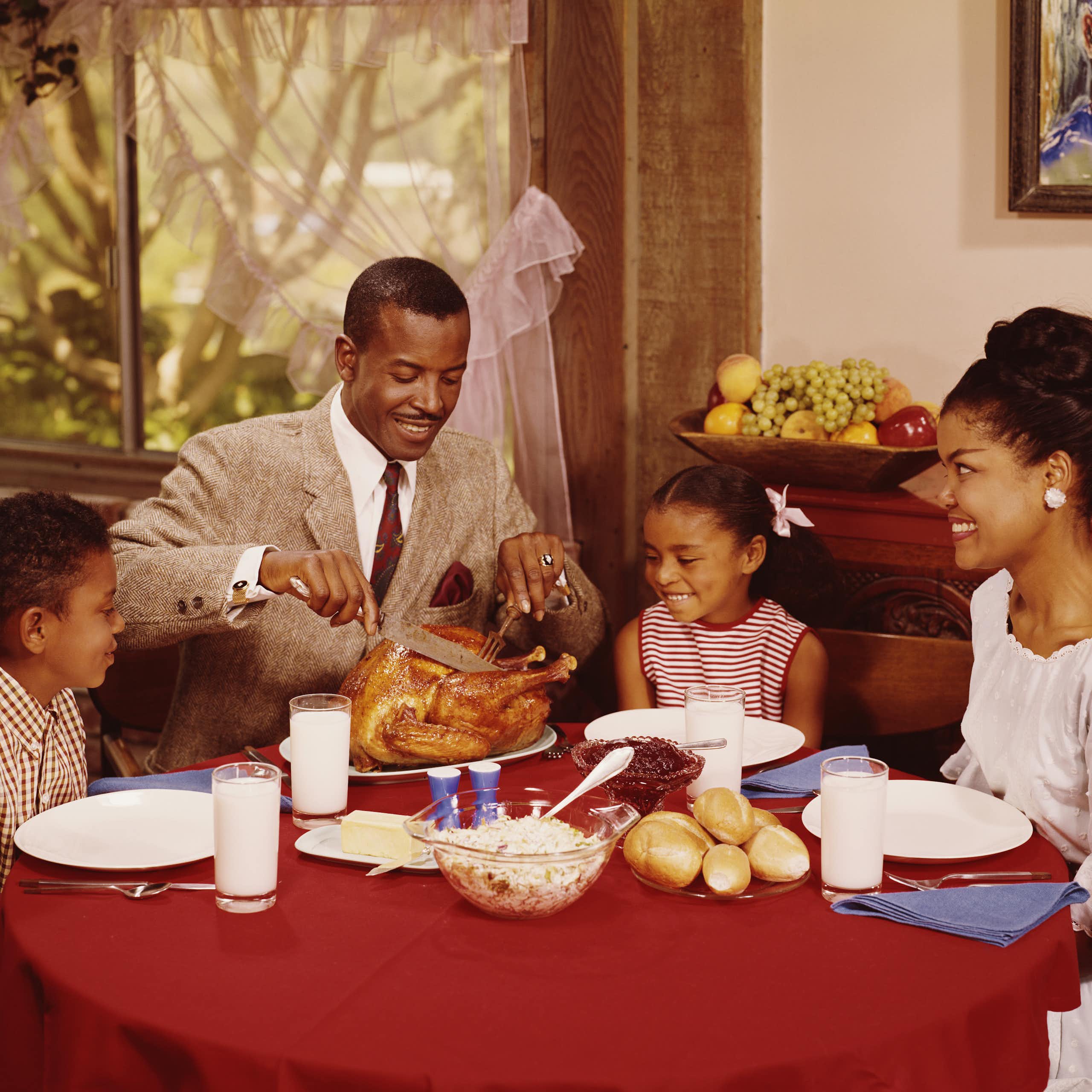 Vintage photograph of a Black family eating dinner – a father, mother and their two young kids. 