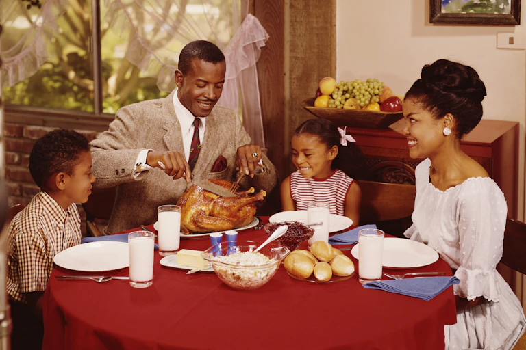 Vintage photograph of a Black family eating dinner – a father, mother and their two young kids.