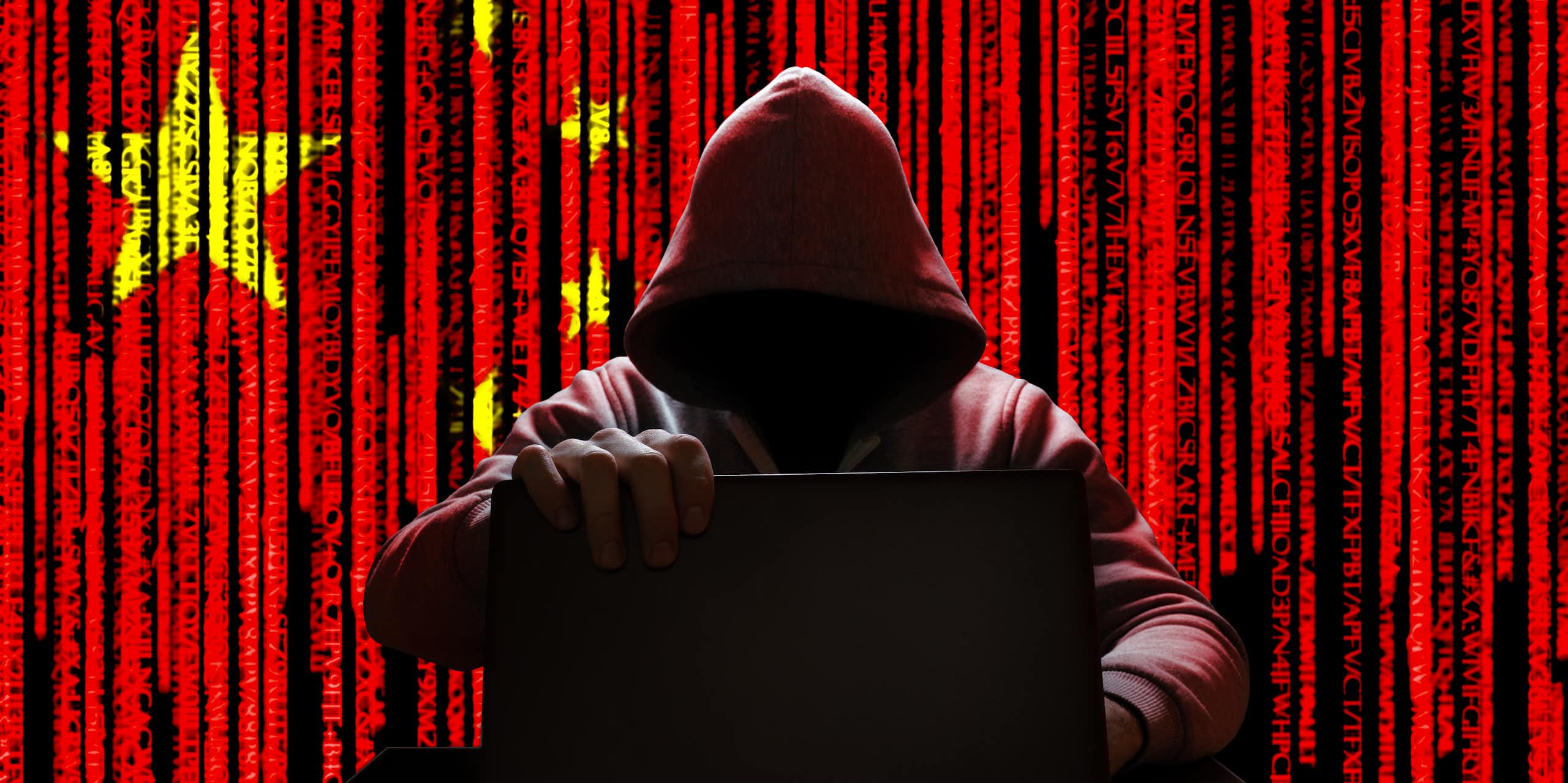 An image of a hooded man holding a laptop against the background of a Chinese flag.