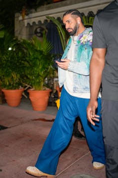 A Black man wearing blue jeans is walking with his hand on an electronic devise.