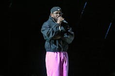 A black man stands on a stage and holds a microphone in his hand.