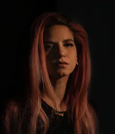 A woman with long hair and a black shirt seen under dim lighting in a portrait.