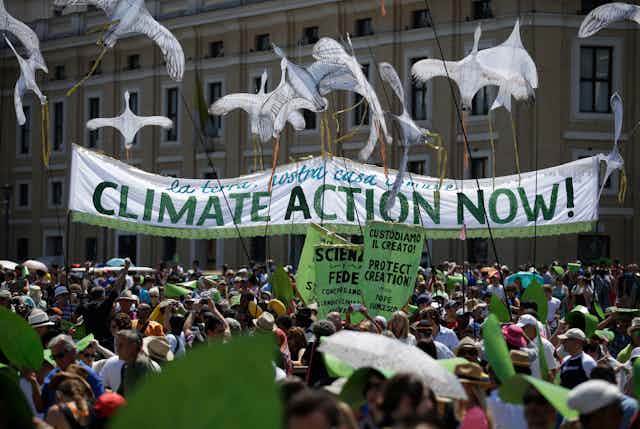 People outside an ornate building hold a sign that says 'Climate action now!'