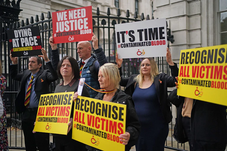 People demonstrate as relatives of victims of the NHS infected blood scandal hand in a letter to 10 Downing Street
