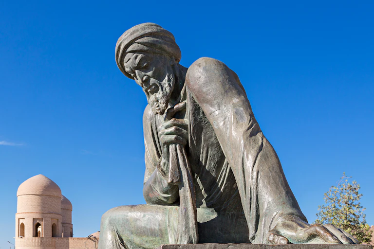 Uma figura de pedra cinza com traços esculpidos e um turbante em um cenário de céu azul.
