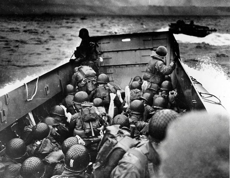 A black-and-white image shows helmeted soldiers jammed into a small watercraft heading through rough seas.