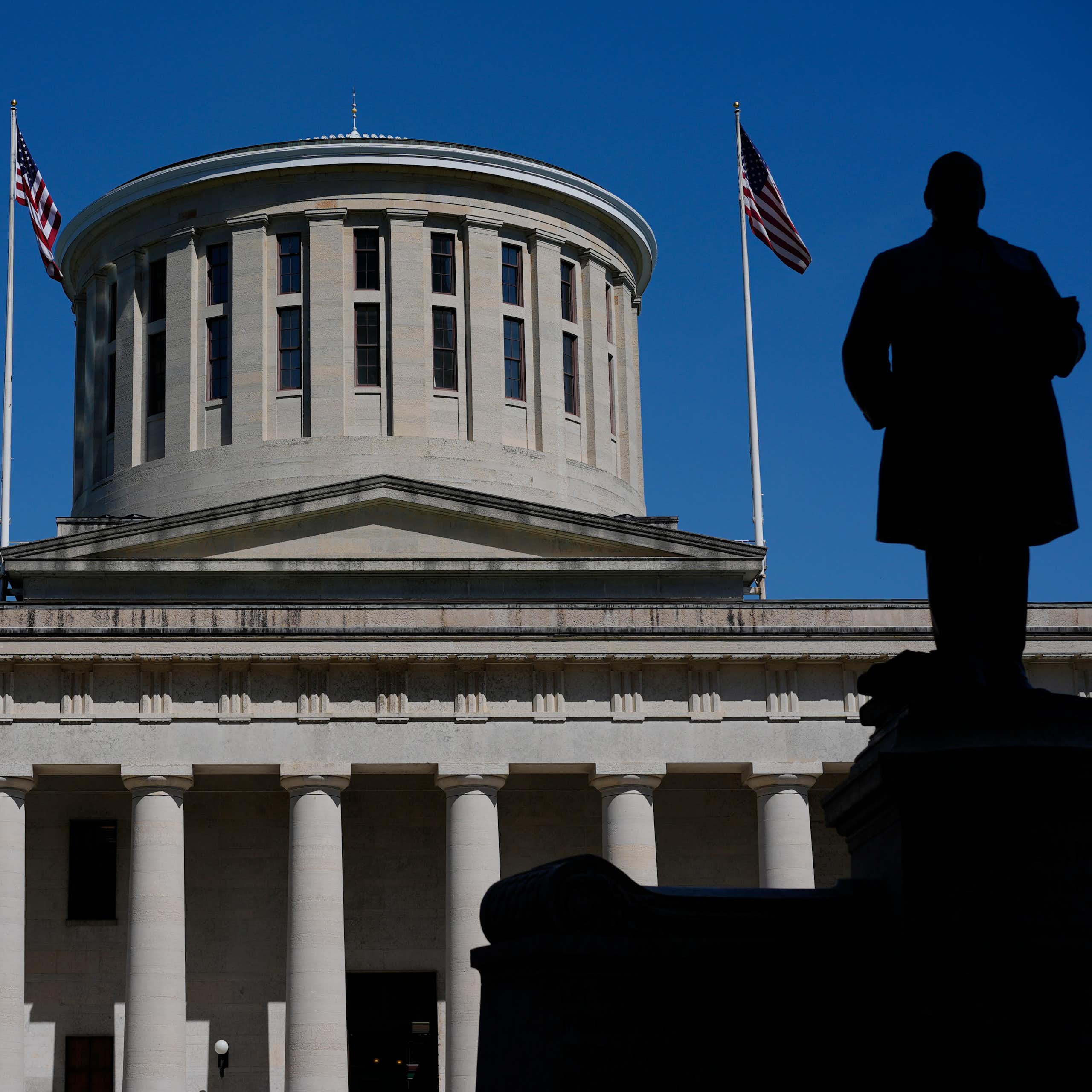 A statue of a man silhouetted against a large gray building with columns and a dome.