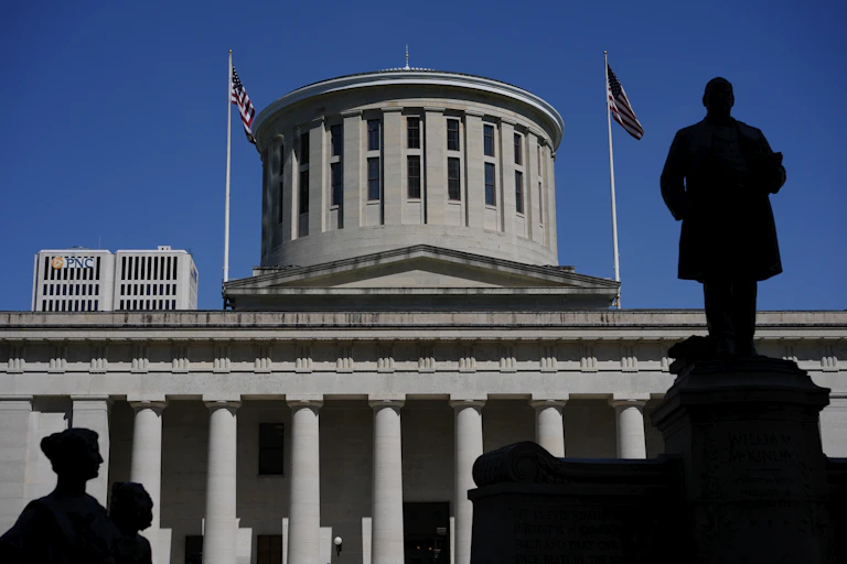 A statue of a man silhouetted against a large gray building with columns and a dome.