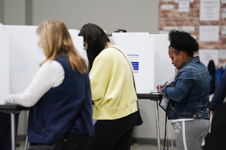 Three women stand at voting booths.