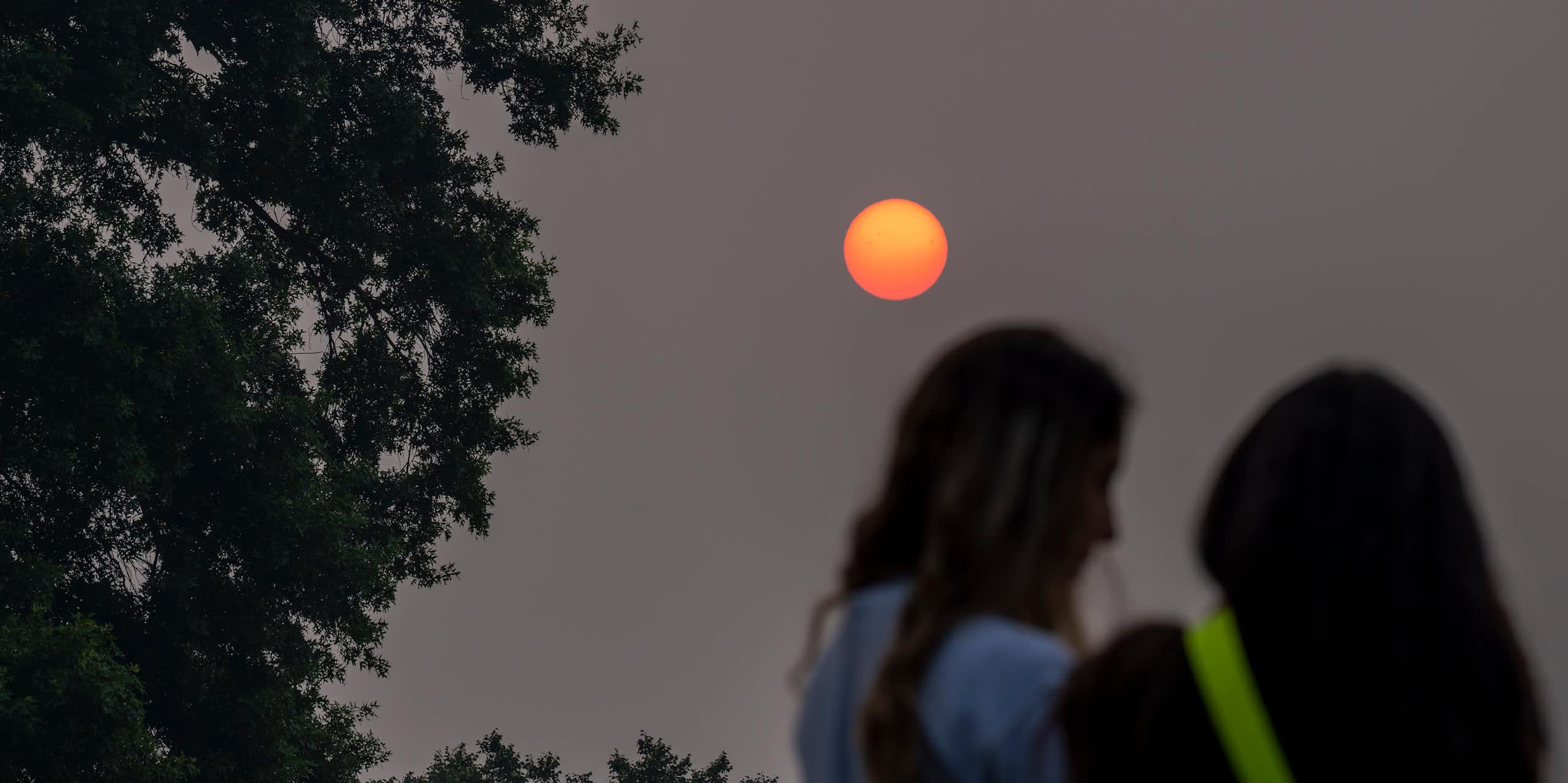 Two people stand under a sun obscured by haze.