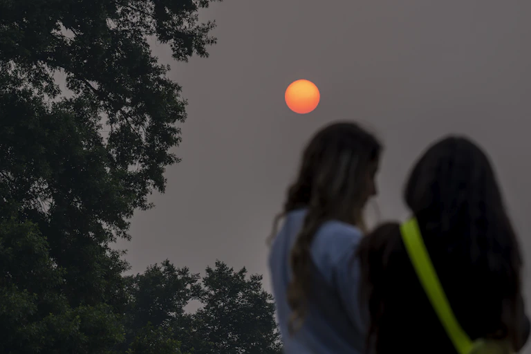 Two people stand under a sun obscured by haze.