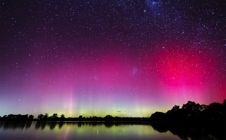 A pink and green sky reflected in still water, stars visible at the top.