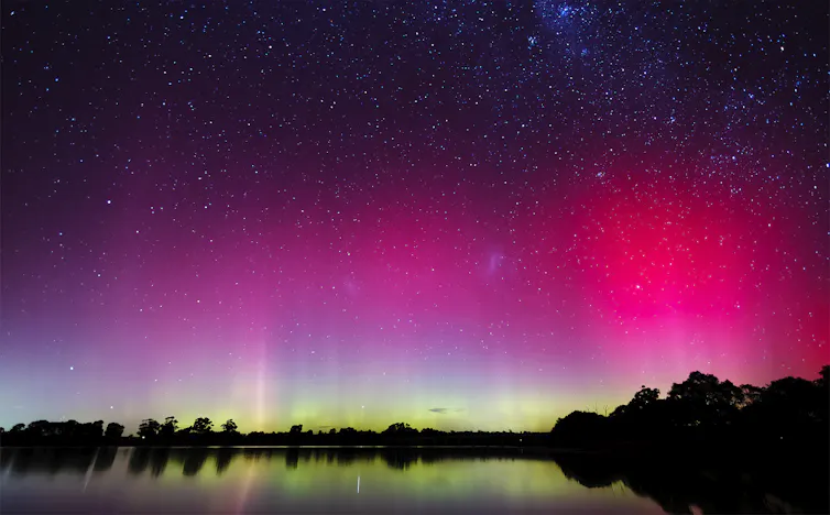 A pink and green sky reflected in still water, stars visible at the top.