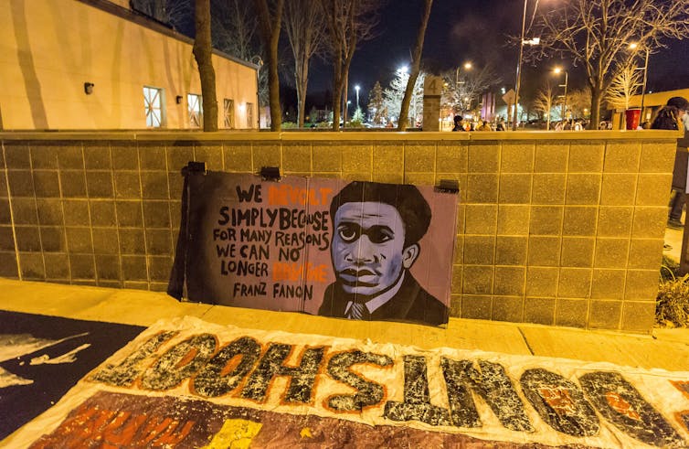 A sign featuring a quote from Frantz Fanon at a protest.