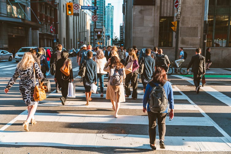 A crowd of people crossing the street at a busy street intersection