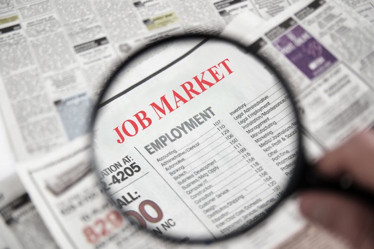 Magnifying glass hovers over a newspaper classified section titled 'Job Market'