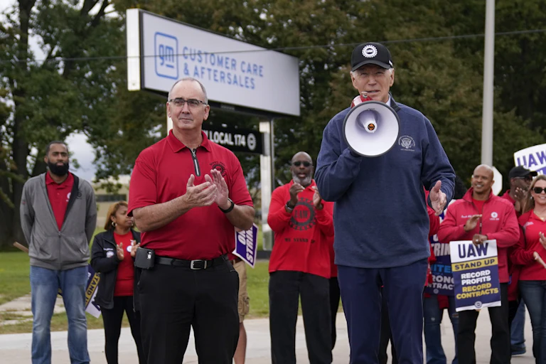 President Joe Biden holds a megaphone, surrounded by people wearing red t-shirts.