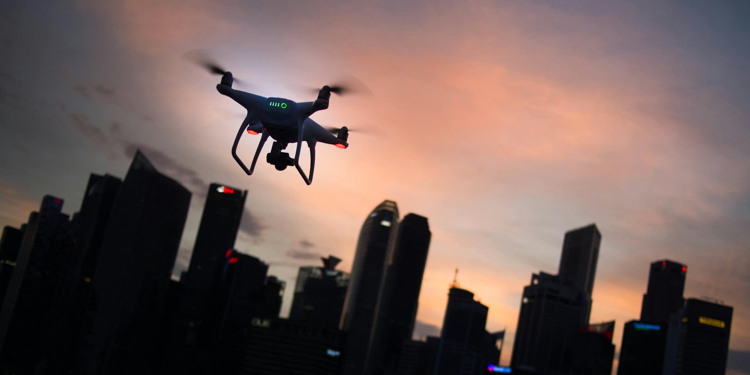 Photo of a quadcopter drone in flight with a city in the background.