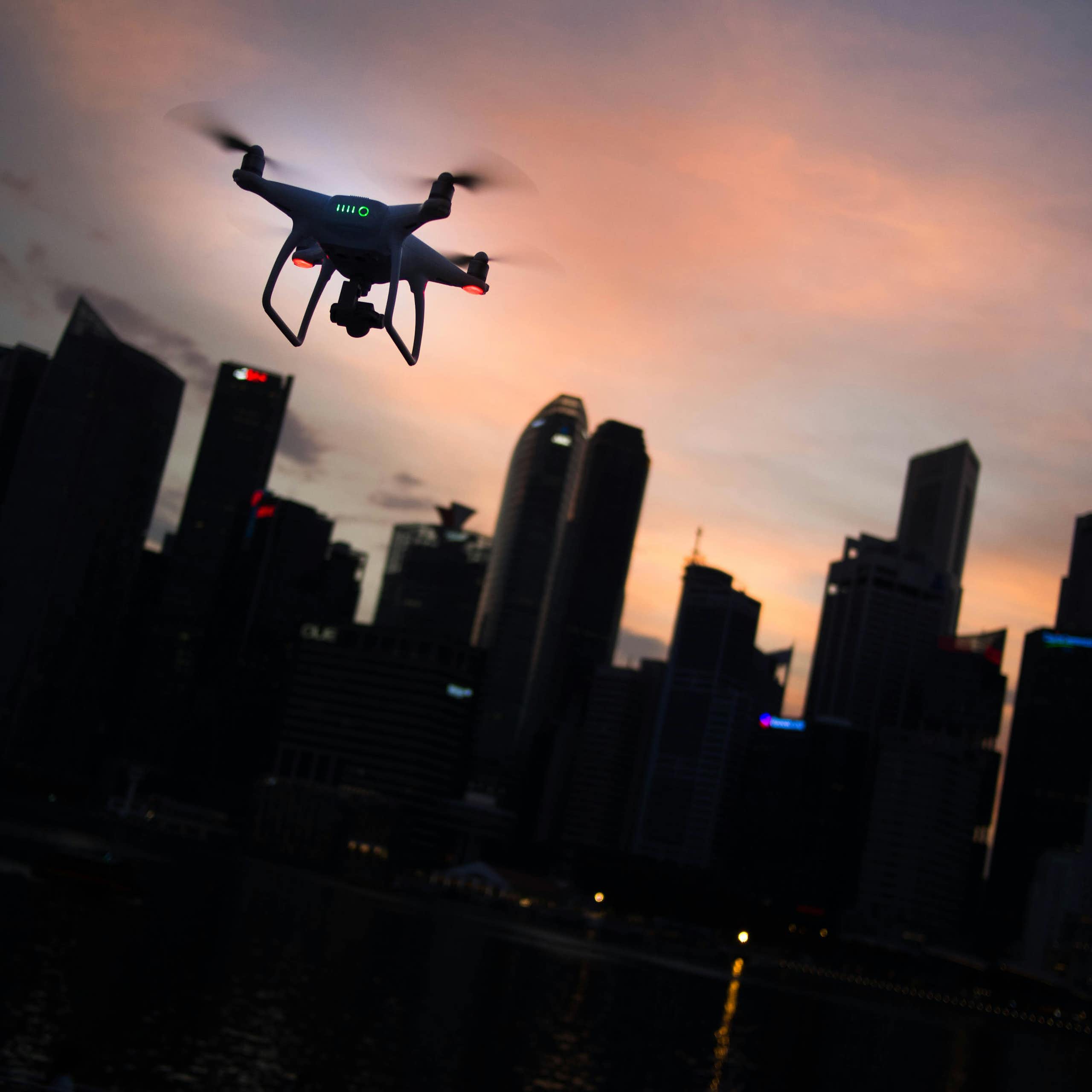 Photo of a quadcopter drone in flight with a city in the background.