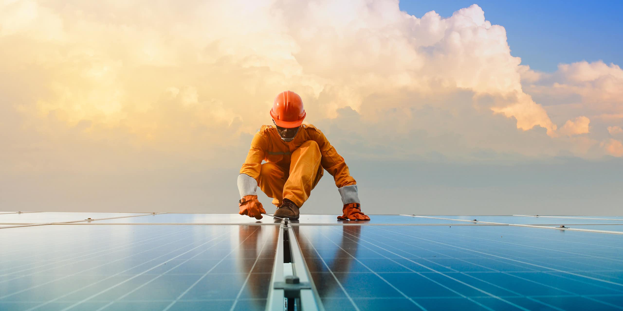 man in hard hat and overalls works on solar panels