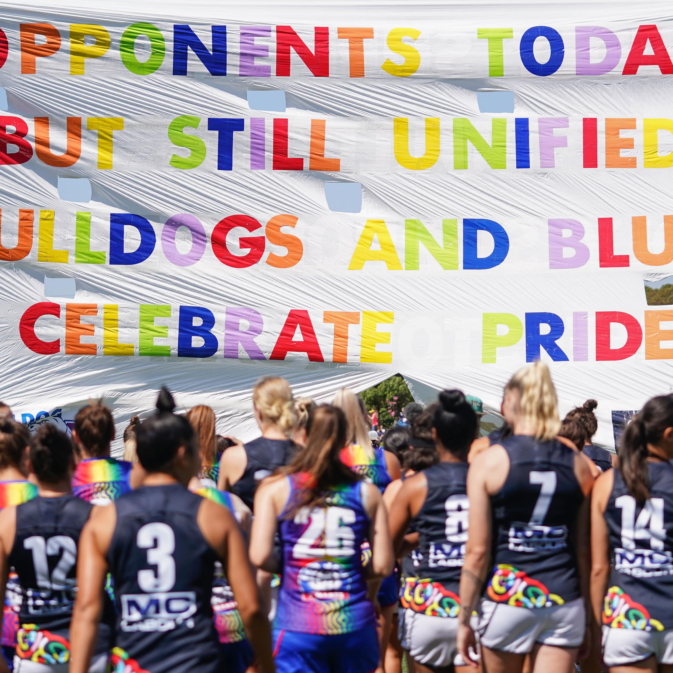 Bulldogs and Blues players run through the Pride banner ahead of an AFLW game