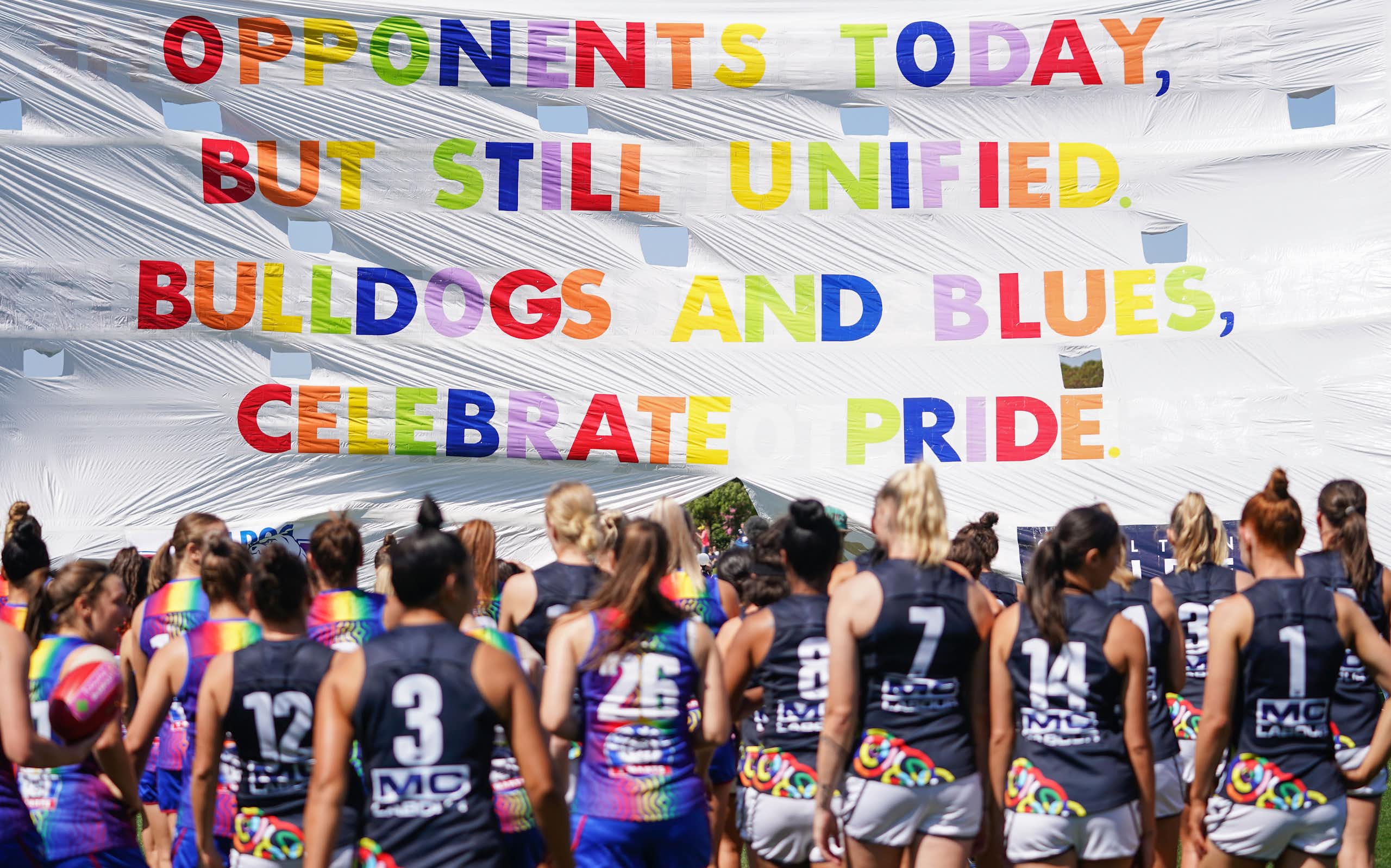 Bulldogs and Blues players run through the Pride banner ahead of an AFLW game