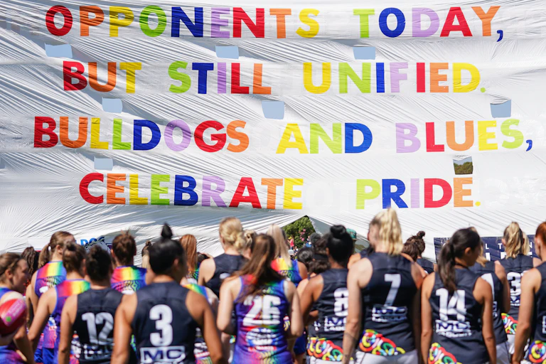 Bulldogs and Blues players run through the Pride banner ahead of an AFLW game