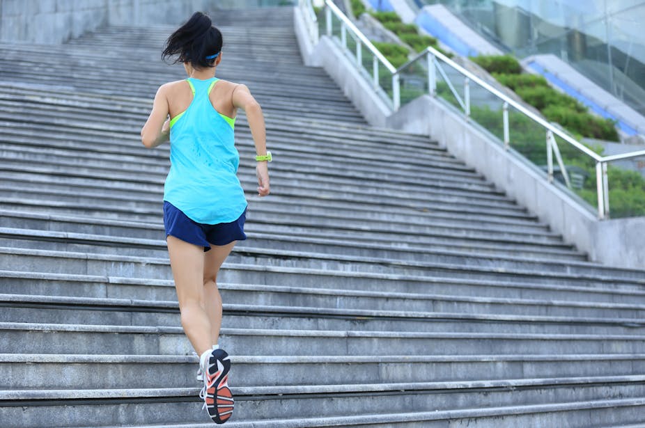 Une jeune femme de dos en tenue de sport monte des escaliers dans un environnement extérieur.