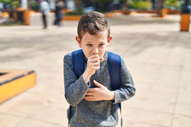 A child wearing a backpack coughs into his closed fist.