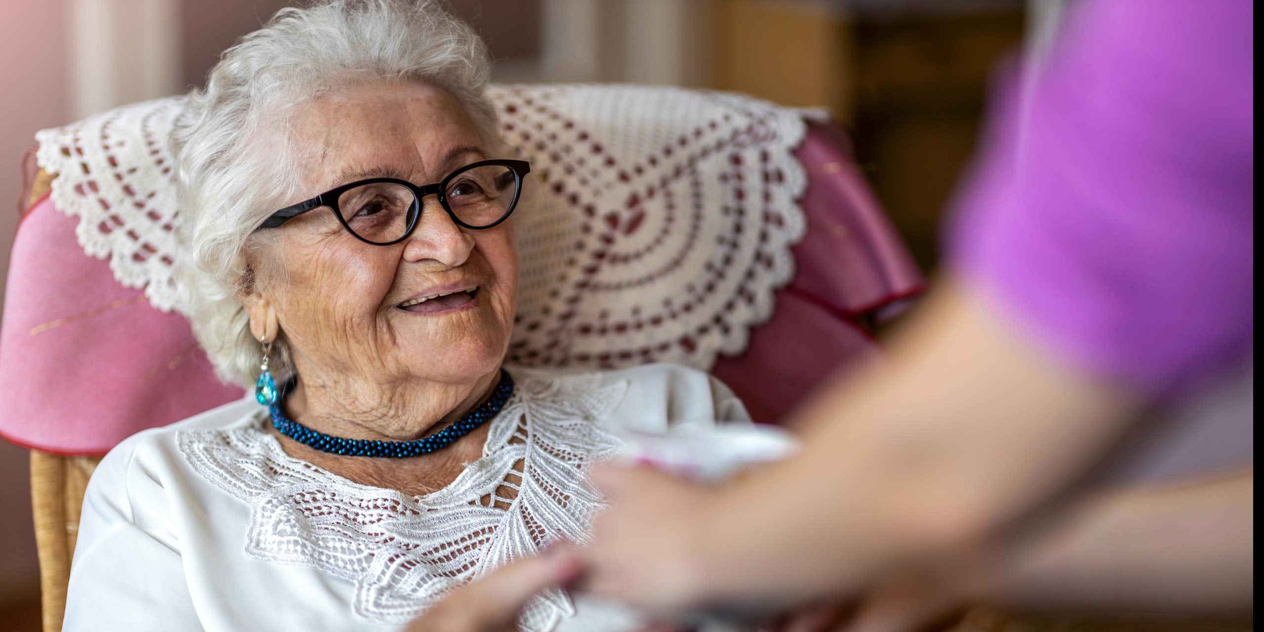 Photo d’une personne âgée souriante dans un fauteuil, tenant les mains d’une autre personne.