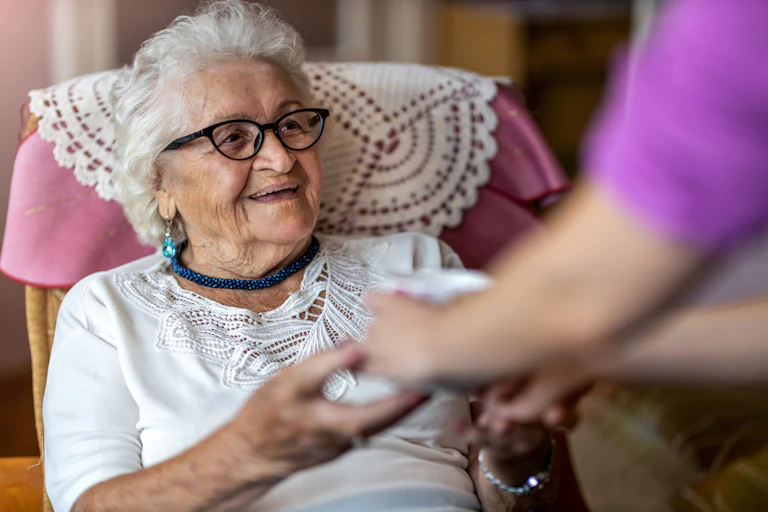 Photo d’une personne âgée souriante dans un fauteuil, tenant les mains d’une autre personne.