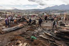 A burnt out area where scores of people look through the rubble to find material to rebuild their shacks