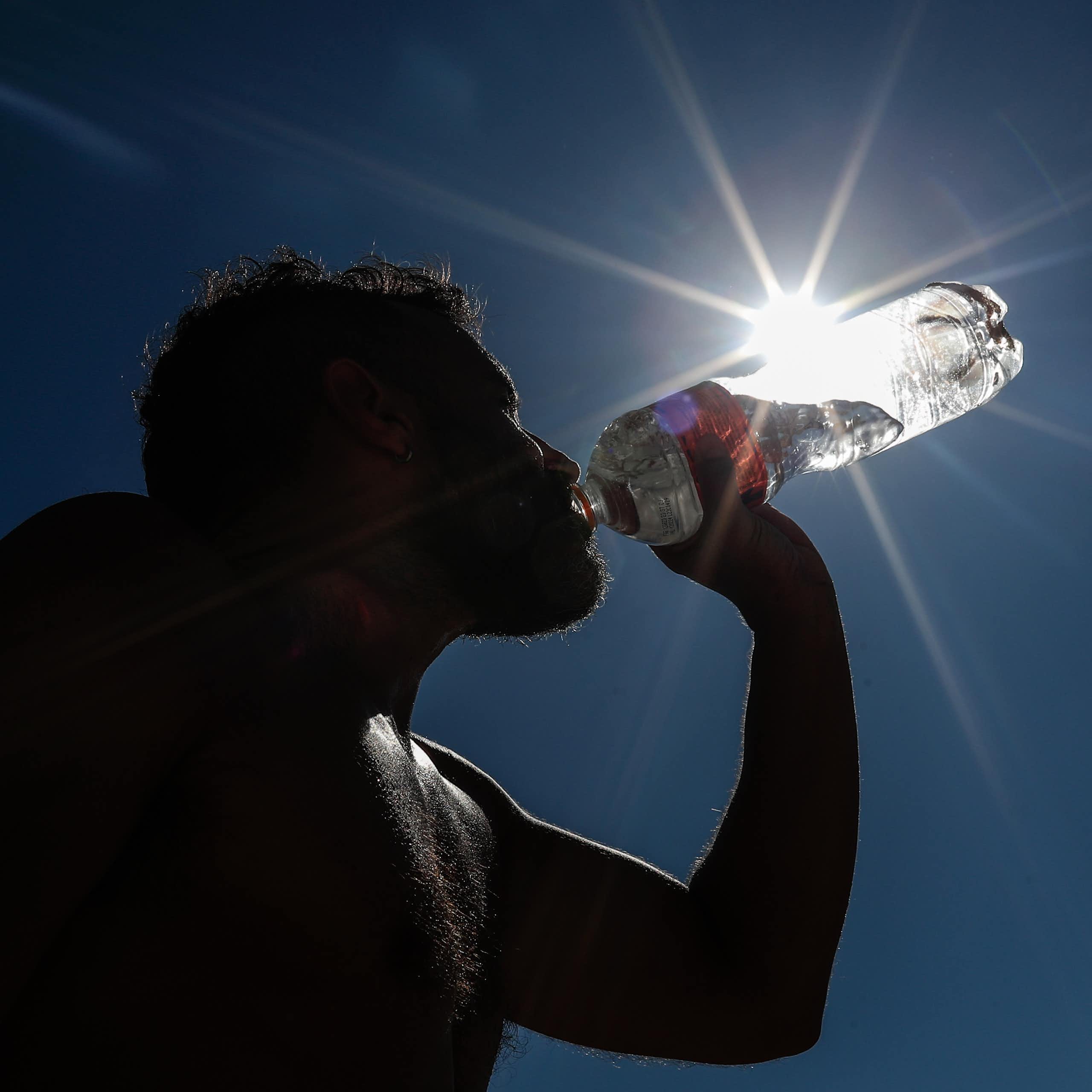 A silhouette of someone drinking water from a plastic bottle.