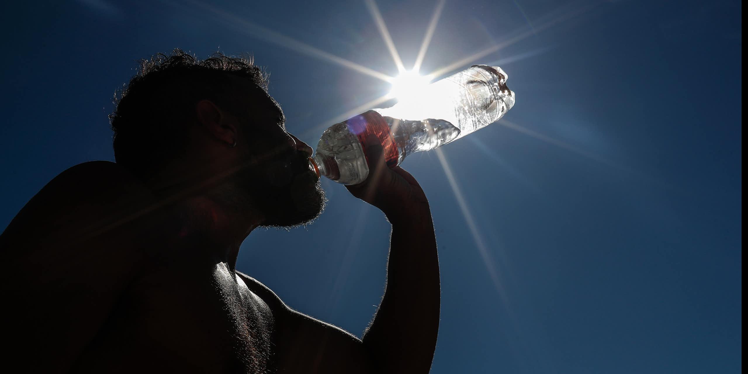 A silhouette of someone drinking water from a plastic bottle.