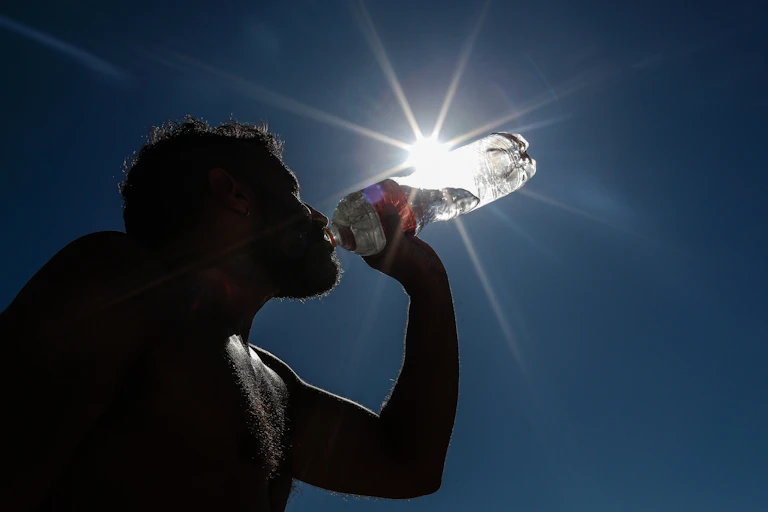 A silhouette of someone drinking water from a plastic bottle.