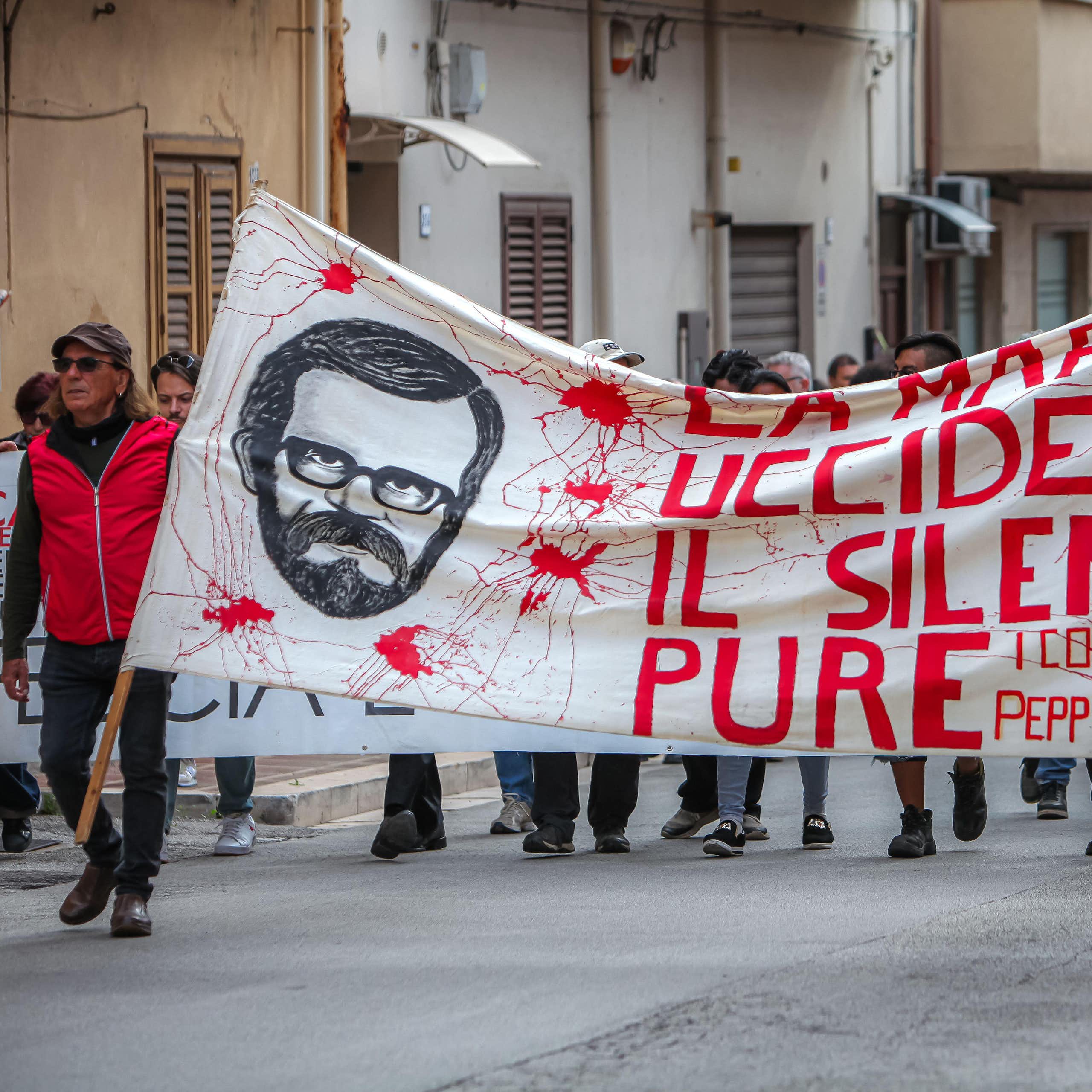 Two men lead a march carrying a banner that reads La mafia uccide il silenzio pure'.