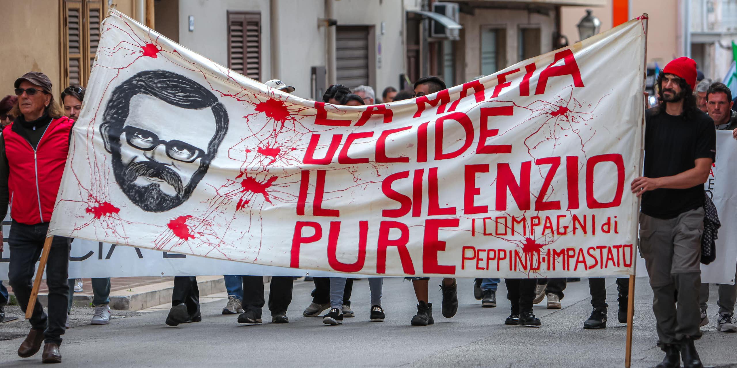Two men lead a march carrying a banner that reads La mafia uccide il silenzio pure'.