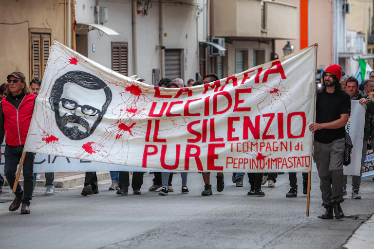 Two men lead a march carrying a banner that reads La mafia uccide il silenzio pure'.