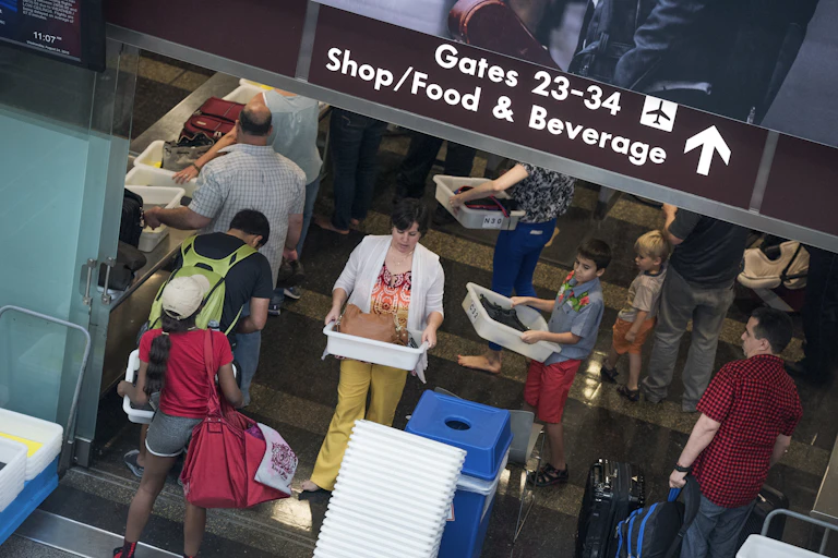 An overhead photograph shows a tangle of people preparing to go through security at Ronald Reagan Washington National Airport. The photograph has a diagonal tilt, which heightens the sense of chaos.