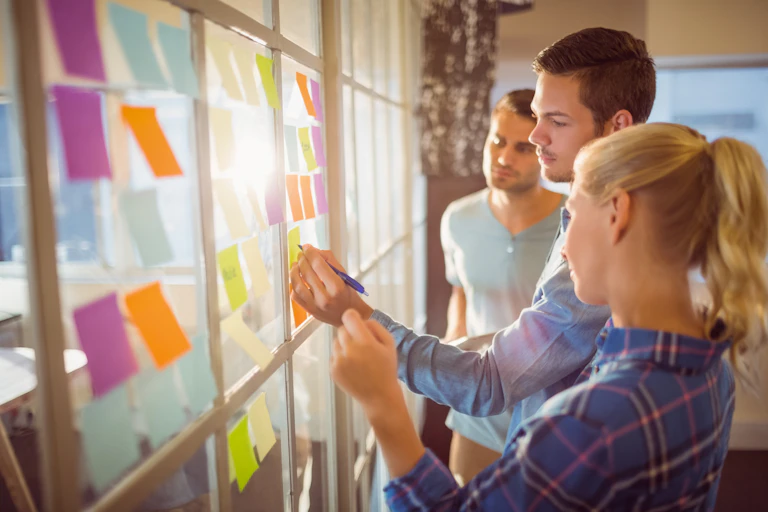 A group of young professionals stand in front of a glass wall covered in sticky notes