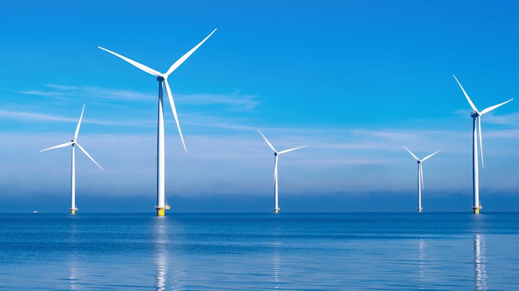 Six big white wind farms out at sea, calm waters, clear blue sky