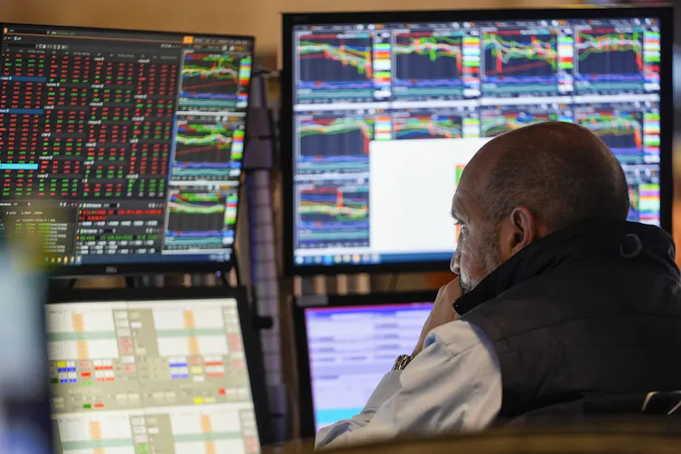 A man sits in front of several large computer screens with many charts on each