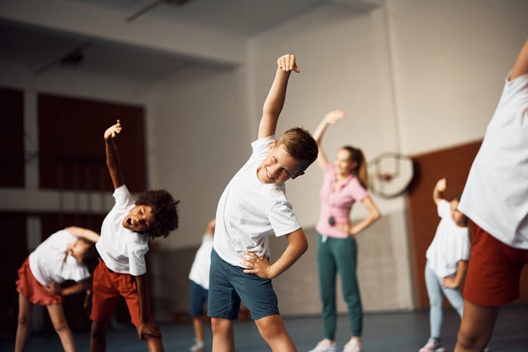 Group of elementary students doing stretching exercises in a school gym