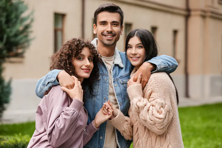 A young man and two young women embrace and pose for a photo together
