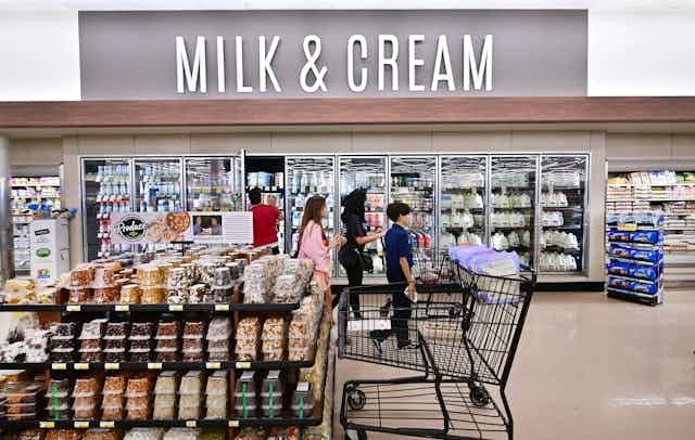 People walk past refrigerated cases under a large sign reading 'Milk & Cream'