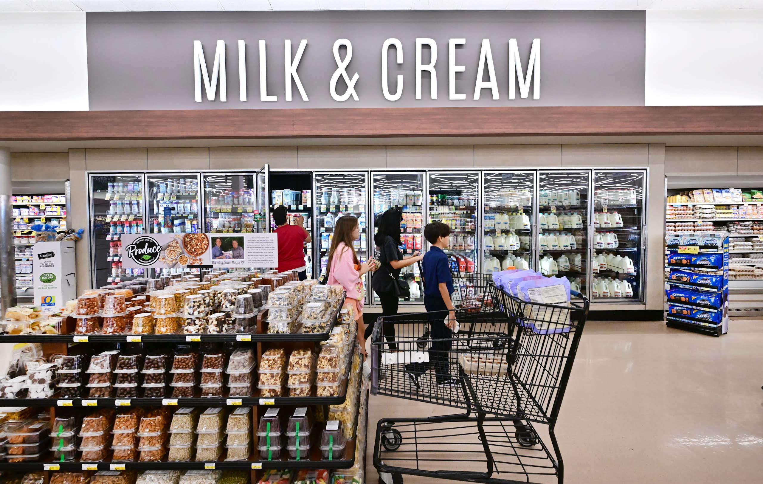 People walk past refrigerated cases under a large sign reading 'Milk & Cream'