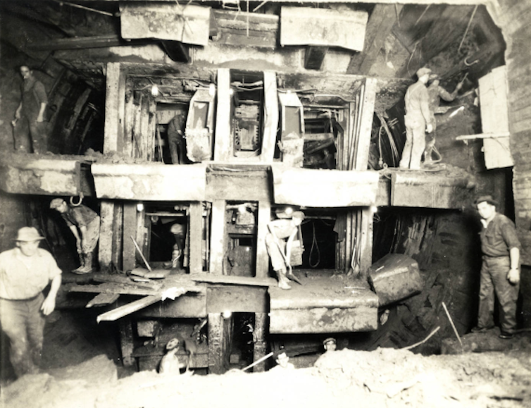 black and white archival photo of men in an enclosed space with what looks like sturdy wooden scaffolding
